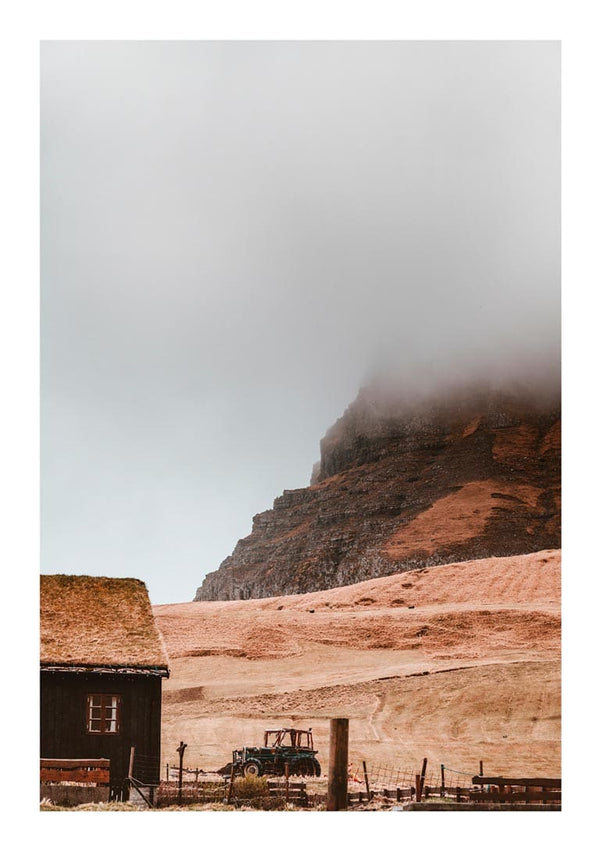 A misty mountain rises behind a rustic field and wooden building, featured on the Cloudy Mountain Plakat product page.