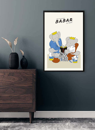 Framed Babar Plakat No. 01 on a dark wall above a wooden dresser with vases and pampas grass.
