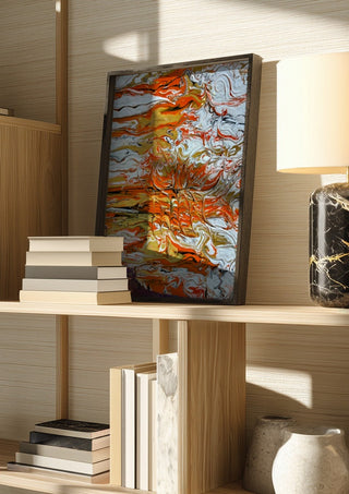 Orange Tide by Da Winters in a dark frame on a wooden shelf beside books and a lamp