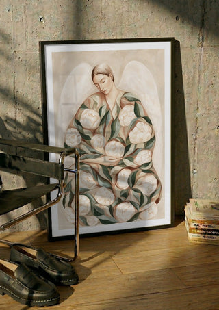 Peony Angel by Martina Karlsson in a black frame leaning against a concrete wall by a steel chair