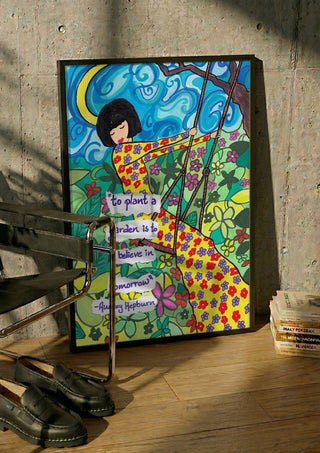 To Plant a Garden by Camilla Nilsson in a black frame leaning against a concrete wall by a steel chair