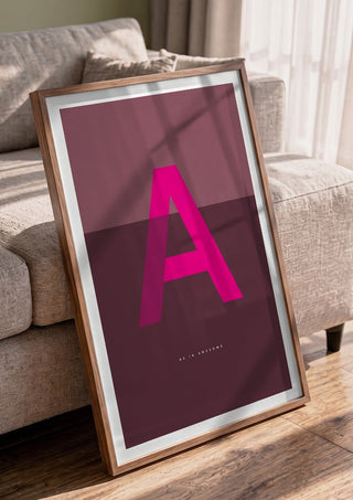 A as in Awesome – Cerise by Quite Nice Prints in a walnut frame leaning against a grey sofa