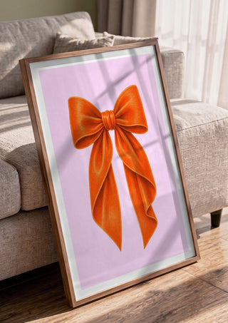 Orange velvet bow on pink by Ohkimiko in a walnut frame leaning against a grey sofa