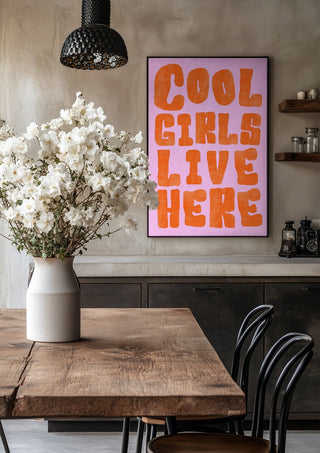 Cool girls live here by Ohkimiko in a black frame above a rustic table with white flowers