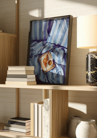 A Cozy Sunday in Bed by Ohkimiko in a dark frame on a wooden shelf beside books and a lamp