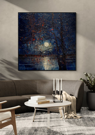 Moon through Bare Trees by Justyna Kopania in a black frame above a dark sofa with candlesticks on a round table
