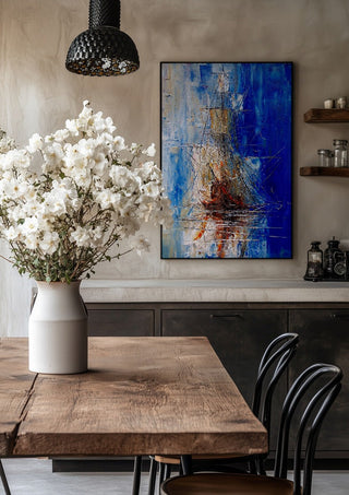 Ship in Blue by Justyna Kopania in a black frame above a rustic table with white flowers