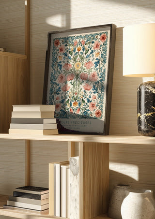 FLEUR PRÉCIEUES by Annika Persson in a dark frame on a wooden shelf beside books and a lamp