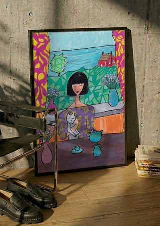 Tea by the Sea by Camilla Nilsson in a black frame leaning against a concrete wall by a steel chair