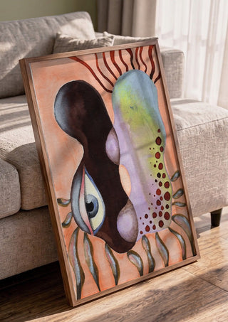 Two Heads, One Eye by Shimmering Ugly in a walnut frame leaning against a grey sofa