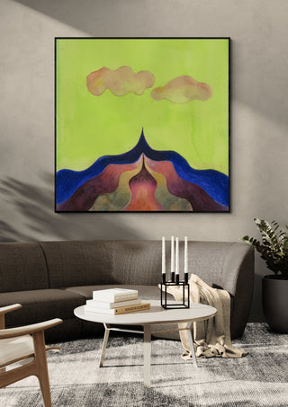 Mountain Under a Green Sky by Shimmering Ugly in a black frame above a grey sofa with a round coffee table