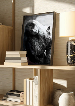 Wind in Her Hair by Bettinafloorphoto in a dark frame on a wooden shelf beside books and a lamp