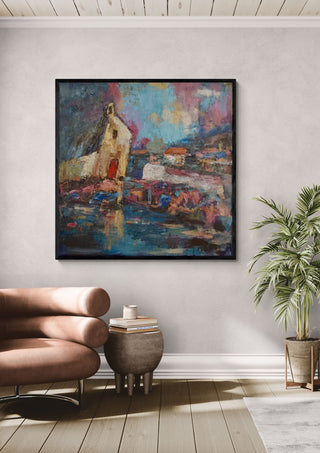 House by the Water by PaKart in a black frame above a pink armchair beside a potted palm