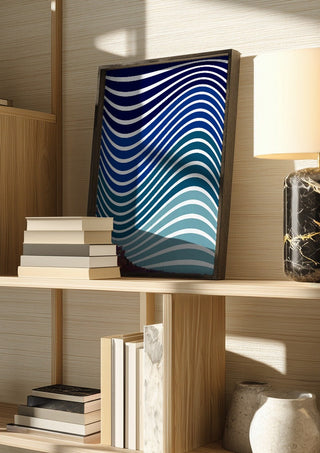 Aallot by Aleksi Allan in a dark frame on a wooden shelf beside books and a lamp