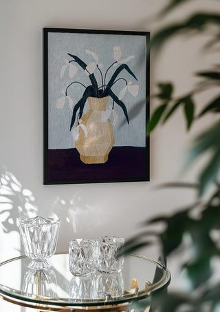 Vita blomster i beige vas by Rebecka Hansson in a black frame above a glass table with crystal glassware
