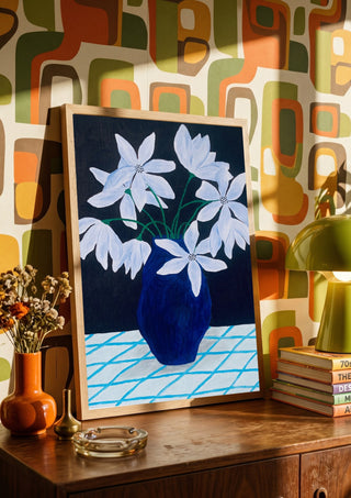 Blå blomster på rutig duk by Rebecka Hansson in a wooden frame on a sideboard against a retro patterned wall