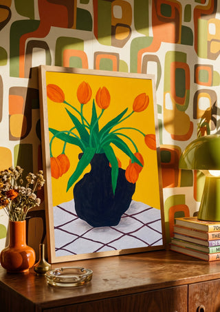 Orangea blomster i brun vas by Rebecka Hansson in a wooden frame on a sideboard against a retro patterned wall