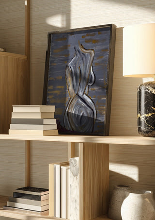 Contours of Silence by Bibi in a dark frame on a wooden shelf beside books and a lamp