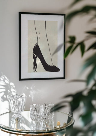 Heavy is the Heel by Nari in a black frame above a glass table with crystal glassware