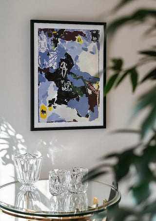 LOVE IS A DOG FROM HELL by Oscar Birch in a black frame above a glass table with crystal glassware