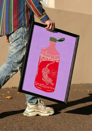 Sriracha chili sauce by Astrid Lind carried in a black frame along a sunny street