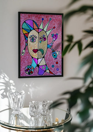 Two Faces and a Crown by Steffi Seiler in a black frame above a glass table with crystal glassware