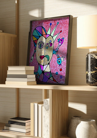 Two Faces and a Crown by Steffi Seiler in a dark frame on a wooden shelf beside books and a lamp