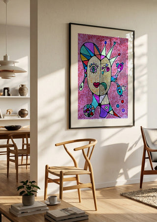 Two Faces and a Crown by Steffi Seiler in a black frame in a bright dining room with wooden chairs