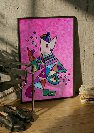 Pink Cat by Steffi Seiler in a black frame leaning against a concrete wall by a steel chair