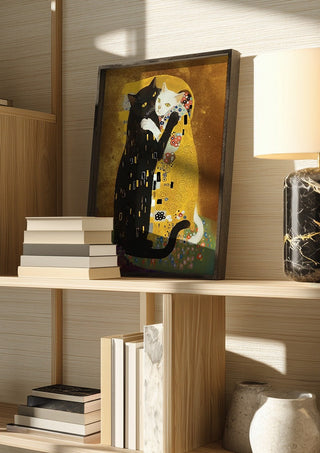 Kitty Kiss by Dikhotomy in a dark frame on a wooden shelf beside books and a lamp