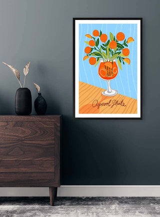 A framed Aperol Plante art print by Nina Broen, featuring orange flowers in a cocktail glass on a wall.