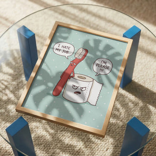 Framed "Grumpy Bathroom Talk" art by Andreas Magnusson on glass table, toothbrush and toilet paper cartoon.