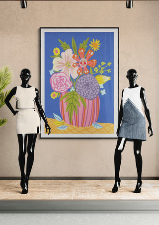 Framed "Blooming" artwork by Nina Broen featuring colorful flowers, displayed behind two mannequins in dresses.