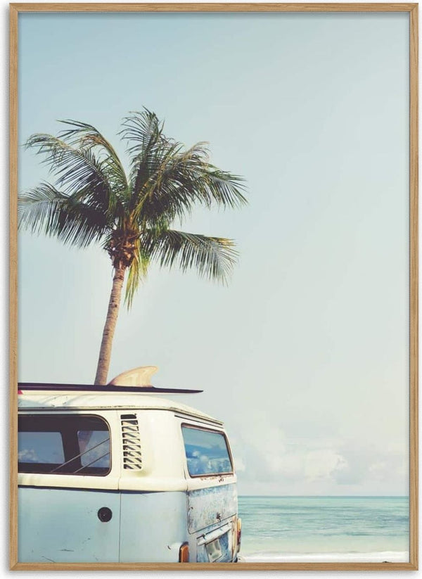 Vintage van with surfboard parked on a beach by the ocean, palm tree in background under clear sky.